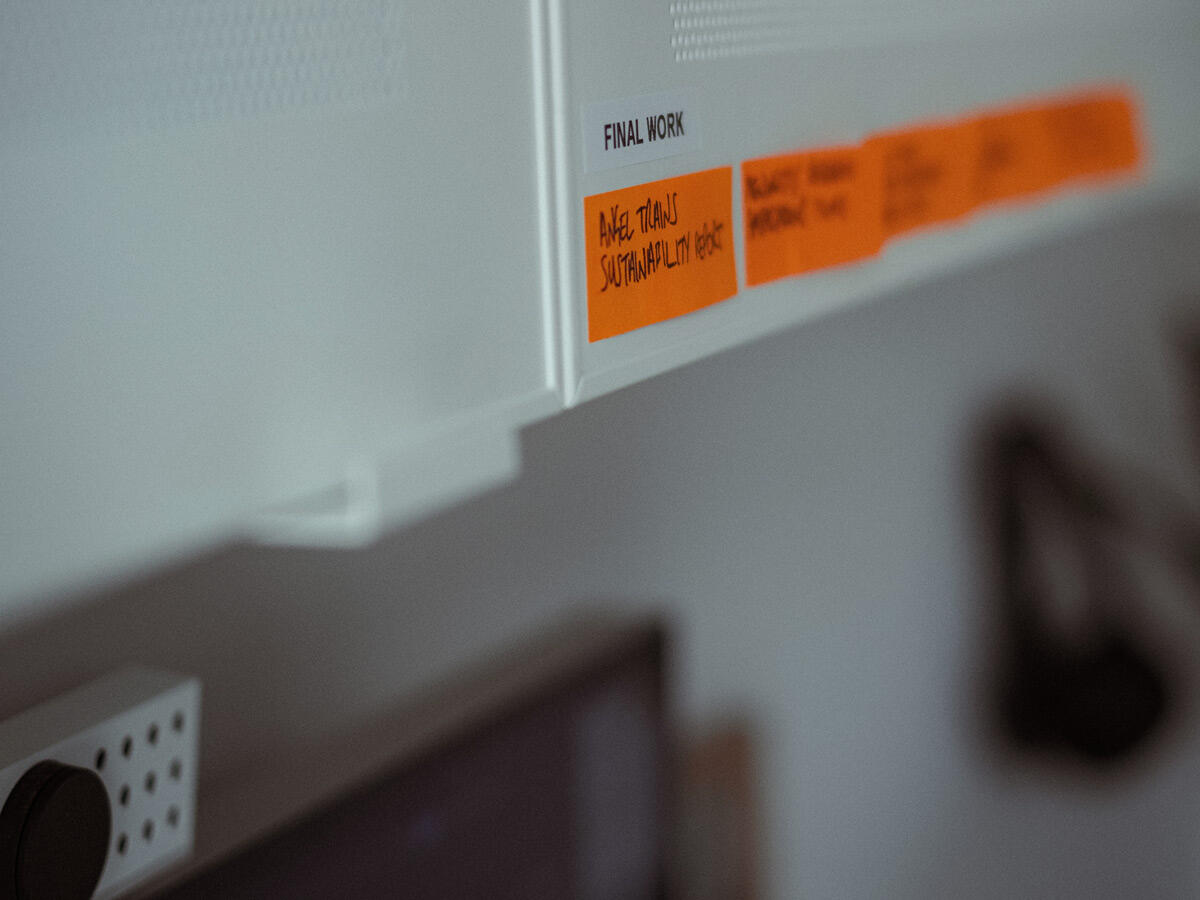 A photograph of Ben sitting in an urban area and looking off-camera. He's wearing winter clothes: a beanie hat, sunglasses, a woolly jumper and a technical coat.