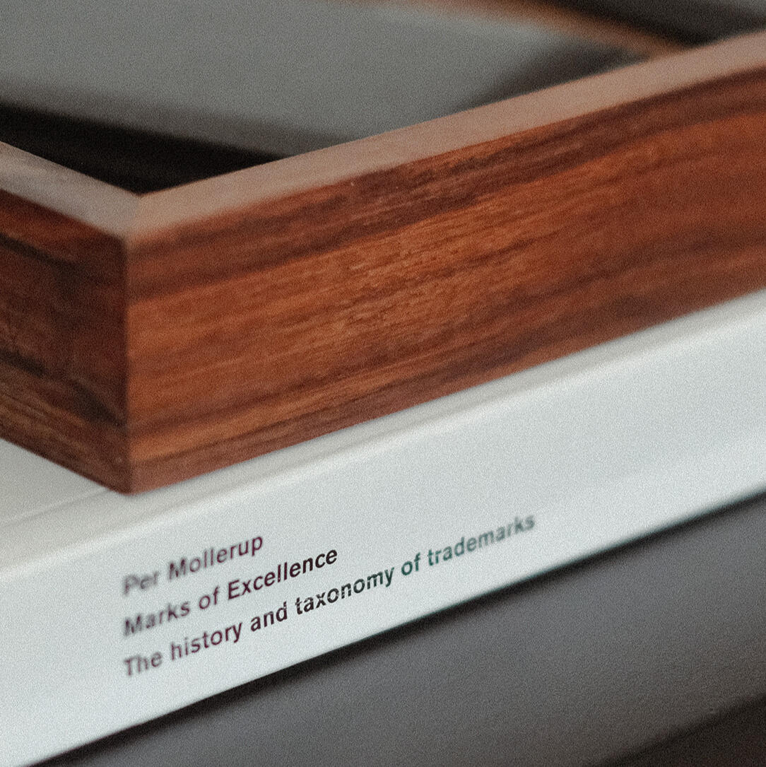 A photograph of a minimal wooden desk in a bright room, featuring a wall-mounted monitor, a tall, potted cactus, and a large, white desktop speaker.